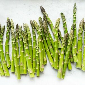 Close up of fresh bright green asparagus on white parchment paper with olive oil and salt.